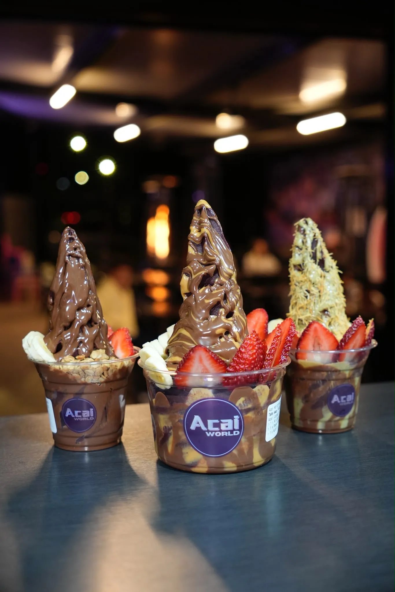 Three Açaí World cups in different sizes with strawberries, granola and sauces